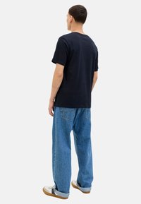 Schwarzes Baumwoll-T-Shirt mit kurzen Ärmeln, kombiniert mit lockeren, hellblauen Jeans. Sneakers mit beigen Sohlen und hochgeschlagenen Säumen.