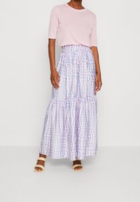 Top rosa chiaro a maniche corte abbinato a una gonna lunga a balze con motivo a quadri pastello in lavanda e azzurro chiaro. Sandali neutri con cinturini.