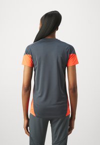Camisa técnica de entrenamiento en gris oscuro con mangas cortas de color naranja brillante. Fabricada con un material que absorbe la humedad, presenta un ajuste relajado y una textura suave.