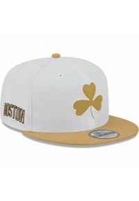 Weiße Mütze mit flachem goldenen Schirm. Verziert mit einem goldenen Shamrock-Logo und "BOSTON" in Schwarz seitlich bestickt. Hergestellt aus strukturiertem Stoff.