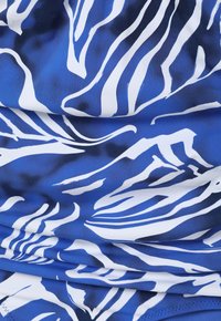 Sinine kangas, millel on julge valge zebra triibuline muster. Materjal on sujuv ja veniv, näidates voltimisest tingitud lainelist tekstuuri.