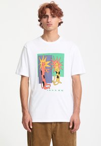T-shirt en coton blanc avec un graphisme coloré de deux chats stylisés sur un fond géométrique. Les détails de l'impression comprennent des couleurs vives et des contours audacieux.
