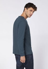 Langärmliges Shirt aus dunkelblauem Baumwollstoff mit rundem Ausschnitt, ausgestattet mit gerippten Bündchen und lässigem Schnitt, kombiniert mit dunklen Jeans.