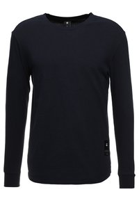 Černé bavlněné tričko s dlouhým rukávem a kulat�ým výstřihem, se malou nášivkou na spodní straně, hladká textura.