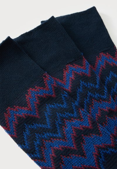 Chaussettes bleu marine foncé avec des motifs en zigzag tricotés rouges et bleus couvrant la moitié inférieure et des bordures bleu marine unies.