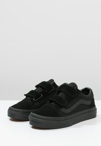 Black suede sneakers with two Velcro straps, round toe, textured rubber sole, and contrasting gray side stripe detail.