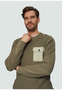 Zielona oliwkowa dzianinowa sweter z teksturowanej tkaniny, okrągłym dekoltem oraz jasnozieloną kieszonką na lewej stronie z czarnym guzikiem.