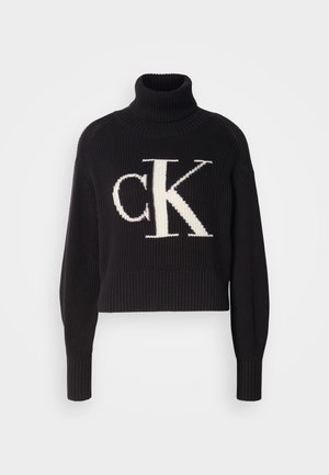 Čierny rebrovaný sveter s vysokým golierom, na prednej strane s veľkým smotanovým logom "ck". Krátka dĺžka a priliehavé rukávy.