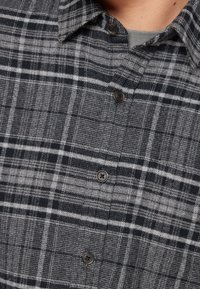 Camisa de cuadros en negro y gris, con cierres de botones, cuello y una tela texturizada con líneas verticales y horizontales.