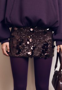 Mini gonna di paillettes con paiette rotonde e riflettenti in tonalità di marrone e viola. Abbinata a collant viola e una borsa scura.