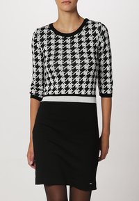 Robe noire et blanche présentant un motif pied-de-poule, coupe ajustée, manches trois-quarts, et une ceinture contrastante. Texture lisse.
