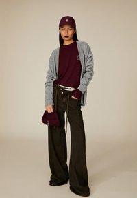 Maroon t-shirt and beanie, gray cardigan, black wide-leg pants, and a matching maroon cap, featuring an embroidered logo. Textured materials.