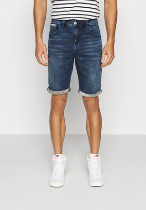 Mørkeblå denimshorts med opblegede kanter, almindelige lommer og glat tekstur. Kombineret med hvide sneakers og en stribet skjorte.