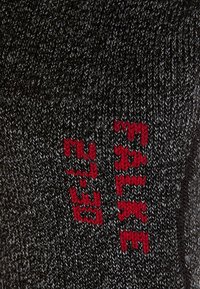 Tela de punto negra con un patrón texturizado, con texto bordado en rojo. El material es suave y elástico, típico de la ropa casual.