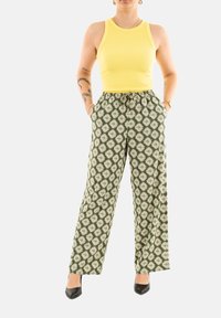 Top giallo a coste abbinato a pantaloni larghi verdi con motivo a rombi. Tacchi neri completano l'outfit.