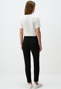 Czarne dżinsowe skinny jeansy z tylnymi kieszeniami, zestawione z białą koszulką z krótkim rękawem. Model w białych sneakersach, widok z tyłu.