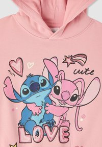 Felpa rosa con un design grafico di due personaggi dei cartoni animati, blu e rosa, circondati da cuori e la parola "AMORE". Materiale in cotone morbido.