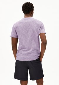 Lichtpaarse T-shirt met korte mouwen en een gestructureerde afwerking, gecombineerd met donkere shorts. Het shirt heeft een ronde halslijn en een labeldetail aan de zijkant.