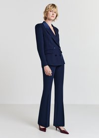 Marineblauer maßgeschneiderter zweireihiger Blazer mit satinierter Klappe, kombiniert mit passenden, taillierten Hosen und glänzenden burgunderfarbenen High Heels.