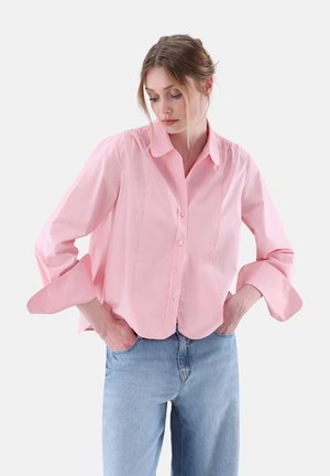 Camicia rosa con colletto e maniche a tre quarti, caratterizzata da una vestibilità comoda e sottili cuciture verticali sul davanti. Abbinata a jeans azzurri chiari.