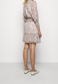 Sukienka w kwiatowy wzór z przezroczystej tkaniny, z marszczonym stanem, falbanami na dole w kilku warstwach oraz długimi rękawami. Noszona z jasnymi butami.