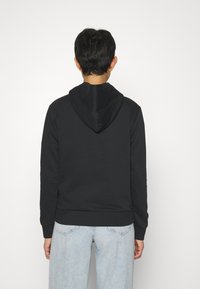 Sweat à capuche noir à texture lisse avec poignets côtelés, associé à un jean bleu clair, présentant une coupe décontractée et un design minimaliste.