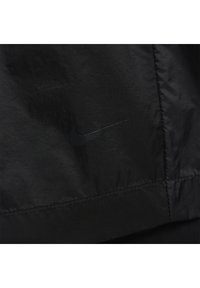 Svart nylonjakt med en subtil svart Nike-logotyp, med en mjuk textur och minimalistisk design. Synliga sömmar accentuerar kanterna.