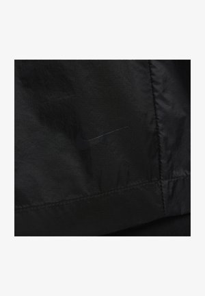 Czarna nylonowa kurtka z dyskretnym czarnym logo Nike, o gładkiej teksturze i minimalistycznym designie. Widoczne szwy akcentują krawędzie.