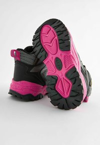 Bottes de randonnée noires et roses avec un dessus texturé et une semelle robuste. La semelle présente un motif rose proéminent pour une meilleure adhérence.