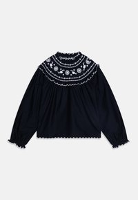 Svart langermet bluse med volangkrage som har hvit blomsterbroderi og scalloped kantdetaljer. Myk bomullsmateriale tekstur.