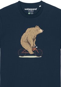 T-shirt bleu marine avec une illustration d'un ours brun faisant du vélo rouge. Le design comprend un ovale couleur crème sous le vélo.