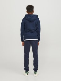 Sudadera azul marino y pantalones de chándal a juego en tela suave, con capucha ajustable y puños acanalados; camiseta blanca debajo y zapatillas.