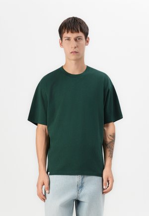 Groene T-shirt met korte mouwen van katoen, met een ontspannen pasvorm en ronde halslijn, gecombineerd met lichtblauwe jeans. Heeft een zijsplit aan de onderkant.