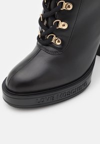 Zwarte leren hoge haklaars met dikke zool met reliëf "LOVE MOSCHINO," zwarte veters door gouden oogjes geregen.