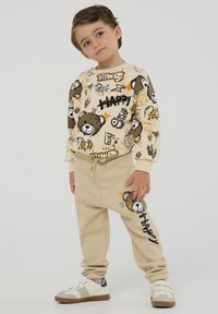 Beżowy dres dla dzieci z wzorzystą kremową bluzą z grafiką niedźwiedzia oraz nadrukiem, w komplecie z dopasowanymi beżowymi spodniami.
