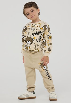 Completo beige per bambini, composto da una felpa crema con un motivo e grafiche di orsetti, abbinata a pantaloni beige coordinati.