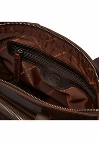 Interieur van een bruine leren tas met een ritsvak, gevoerd met een bruine stof met herhaald terugkerend merklogo. Gladde textuur en gestructureerde vorm.