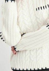 Gruby sweter w splot kablowy w kolorze śmietankowym z ściągaczami. Ciemnoniebieskie akcenty na ściągaczach i dolnym brzegu, z teksturowanym, przytulnym wzorem.