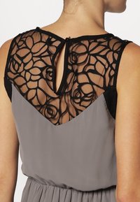 Graues Kleid mit einem schwarzen Spitzenrücken mit floralen Mustern und einem Schlüsselloch-Detail. Glattes Material mit einem fließenden Design.