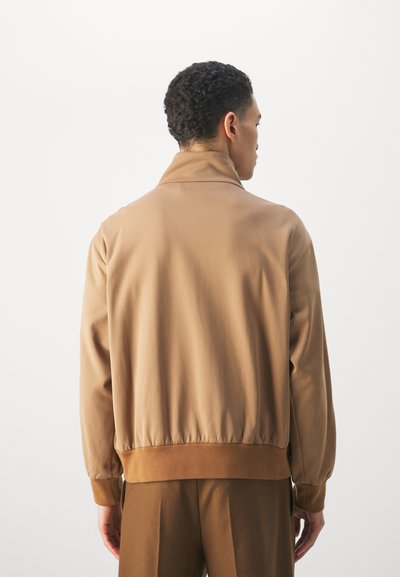 Giacca bomber leggera marrone realizzata in tessuto morbido, con colletto alto e orlo e polsini elasticizzati, caratterizzata da una vestibilità rilassata.