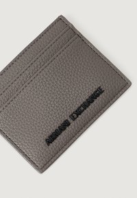 Portafoglio in pelle grigia con texture, logo nero "Armani Exchange" e bordi cuciti su sfondo bianco.