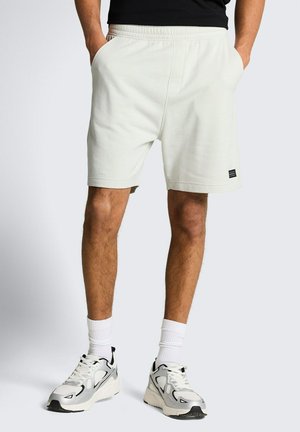 Mann trägt weiße Shorts mit elastischem Bund und Seitentaschen, weiße Crew-Socken und weiße Sportschuhe mit schwarzen Akzenten.