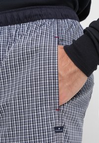 Shorts à carreaux bleu marine et blancs avec une taille élastique, une poche latérale et une petite étiquette avec le logo. Tissu en coton texturé.