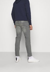 Pánské šedé džíny s úzkým střihem a jemným vyblednutím. Mají dvě zadní kapsy s dekorativním šitím. Kombinovány s námořnicky modrou mikinou s kapucí a bílými teniskami.