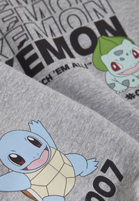 Tessuto di cotone grigio che presenta i personaggi Pokémon Bulbasaur e Squirtle, con testo nero in grassetto e colori vivaci per i design dei personaggi.