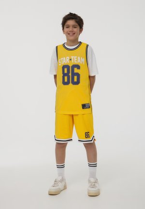 Żółta sportowa koszulka z siateczkową teksturą, z napisem "STAR TEAM" i numerem "86" w niebieskim kolorze. Żółte szorty w koordynującym kolorze, z czarno-białymi paskami.