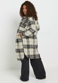 Kariertes Flanellhemd-Jacke in Creme, Marineblau und Oliv, mit großen Knöpfen, seitlichen Taschen und einem leicht geschwungenen Saum.