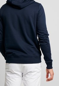 Granatowy hoodie z mieszanki bawełny z kapturem na sznurku, ściągaczami przy mankietach i u dołu. Charakteryzuje się gładką teksturą i minimalistycznym designem.