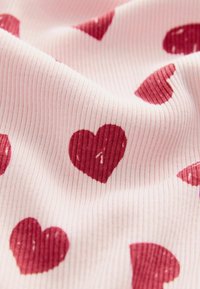 Tissu côtelé rose avec motifs de cœurs rouges, présentant une texture lisse et des designs espacés régulièrement. Idéal pour les vêtements décontractés ou les articles d'ameublement doux.