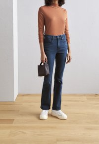 Bränd orange långärmad topp, högmidjade mörkblå jeans, vita sneakers och en liten brun handväska med handtag.